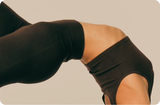 Close-up of a person wearing black ribbed athletic leggings and a matching black cutout sports bra against a plain beige background.