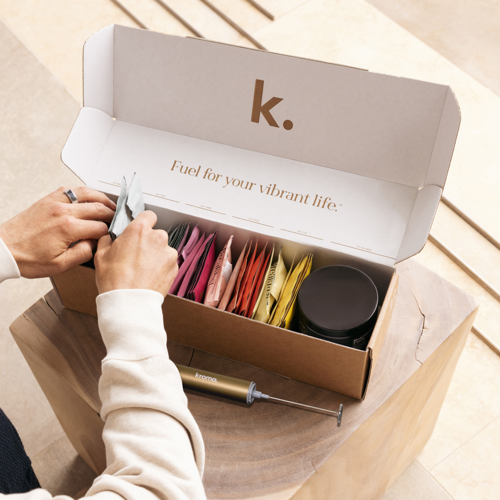 Person opening a Kroma Reset box of sachets with colorful packets and a black container of OMG Cookie Butter.